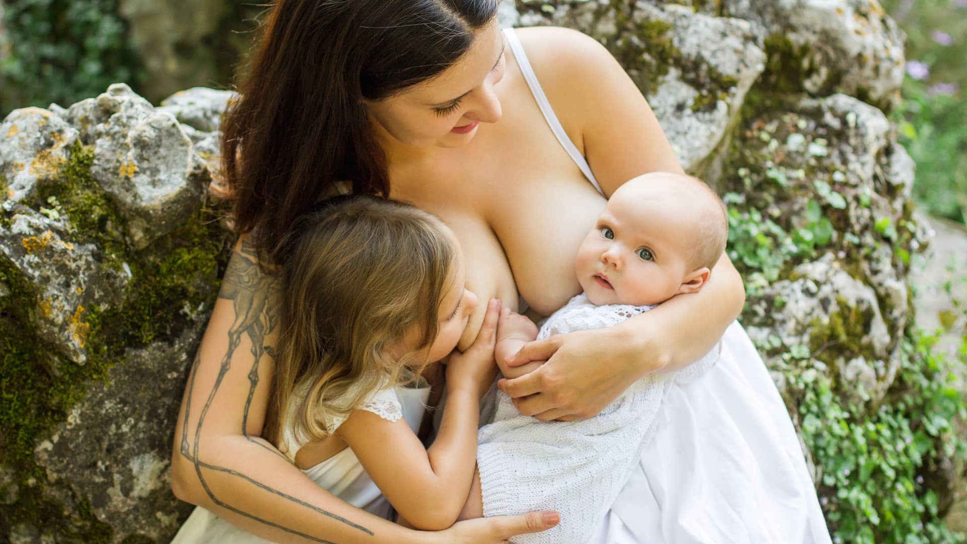 Chica dando la lactancia materna tandem a su bebé y a su hija mayor a la vez