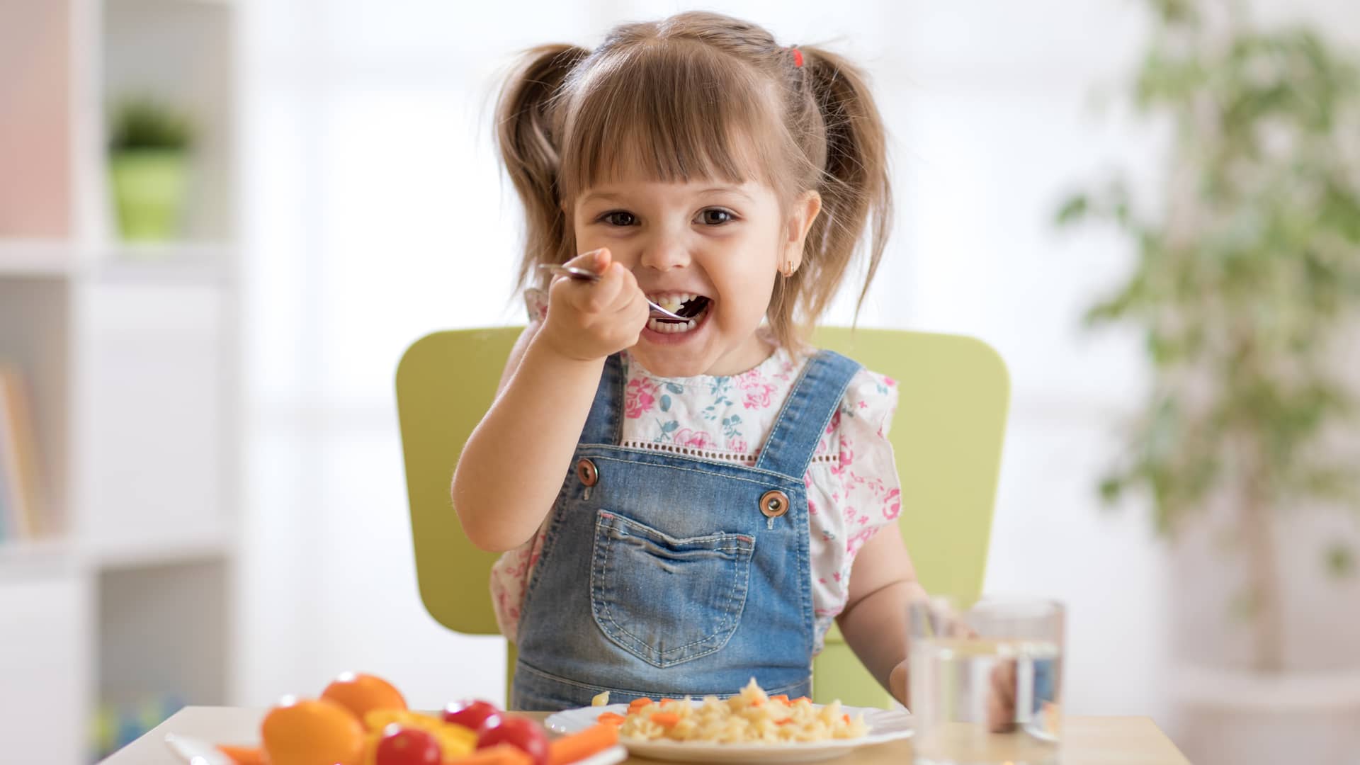 niña muy pequeña comiendo sola un menu infantil sano y adaptado a su edad para que crezca sana