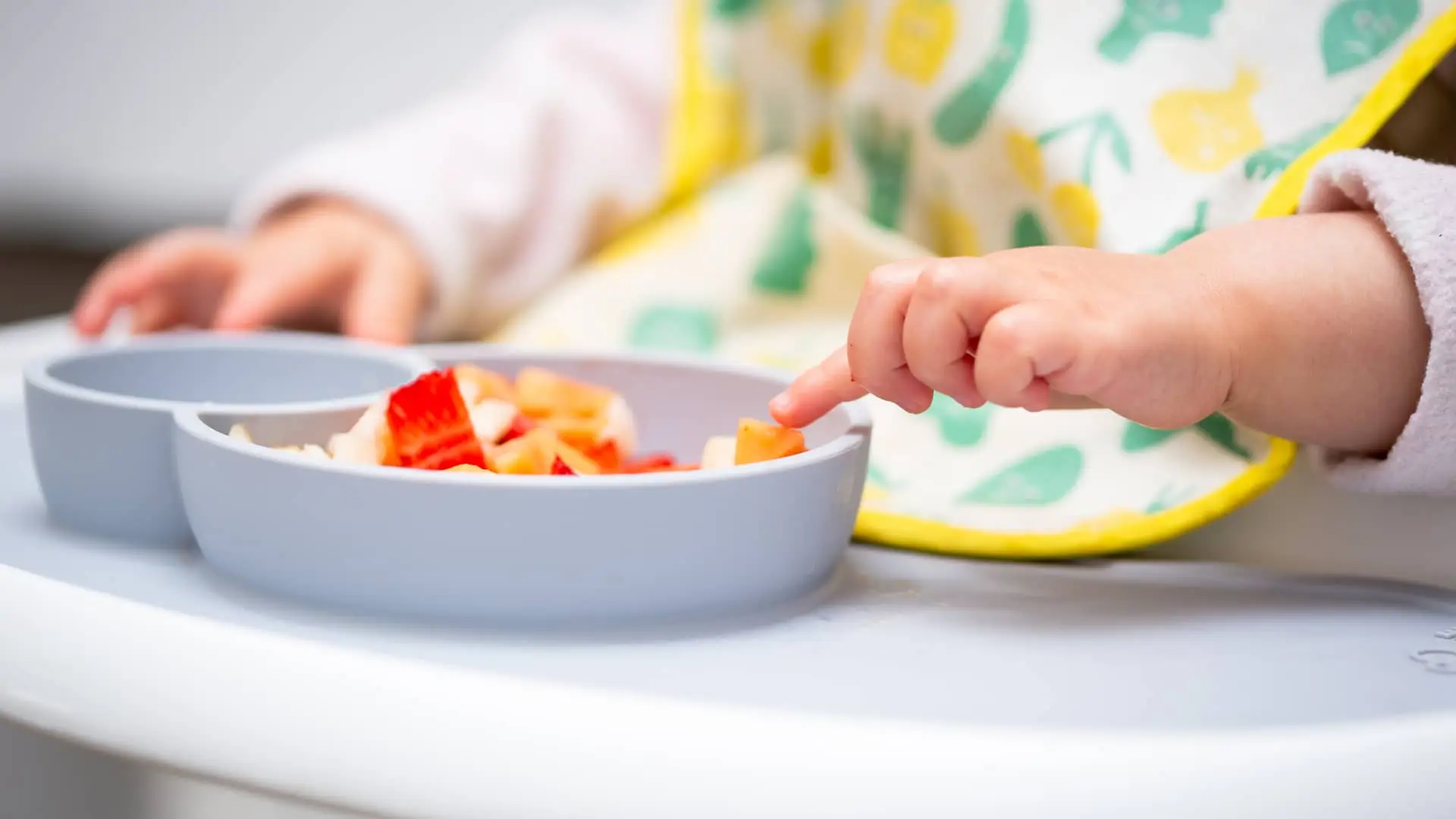 Manos de bebe tocando trozos de frutas como parte de una correcta alimentación infantil