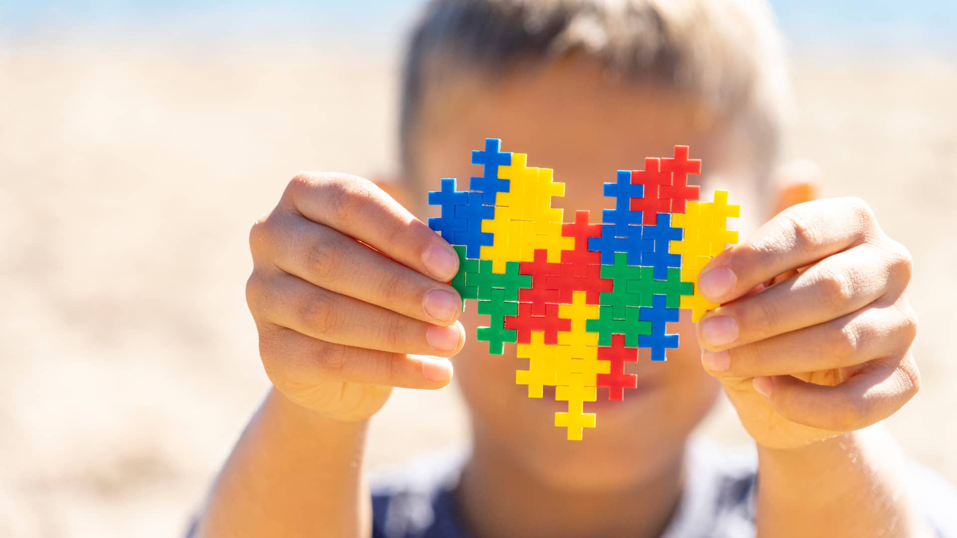 Niño sosteniendo un corazón hecho con piezas de puzzle, símbolo del autismo infantil