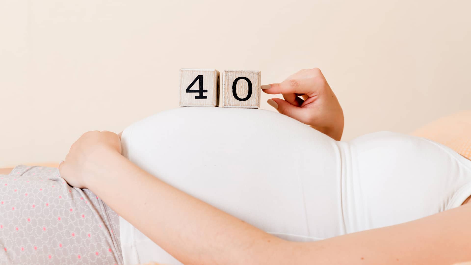 Mujer luce su barriga de 40 semanas de embarazo junto a unos dados que indican los números
